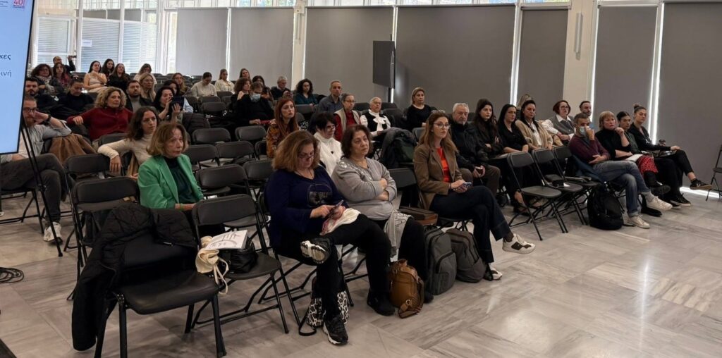 Συμμετέχοντες καθισμένοι στο ακροατήριο συνεδριακής αίθουσας.